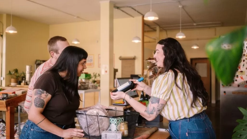 formas de fidelizar o cliente: vendedora mostrando garrafa de vinhos para casal de clientes.