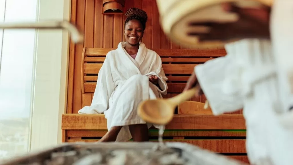 casal em sauna enquanto homem coloca essência em pedras quentes para exalar aroma.